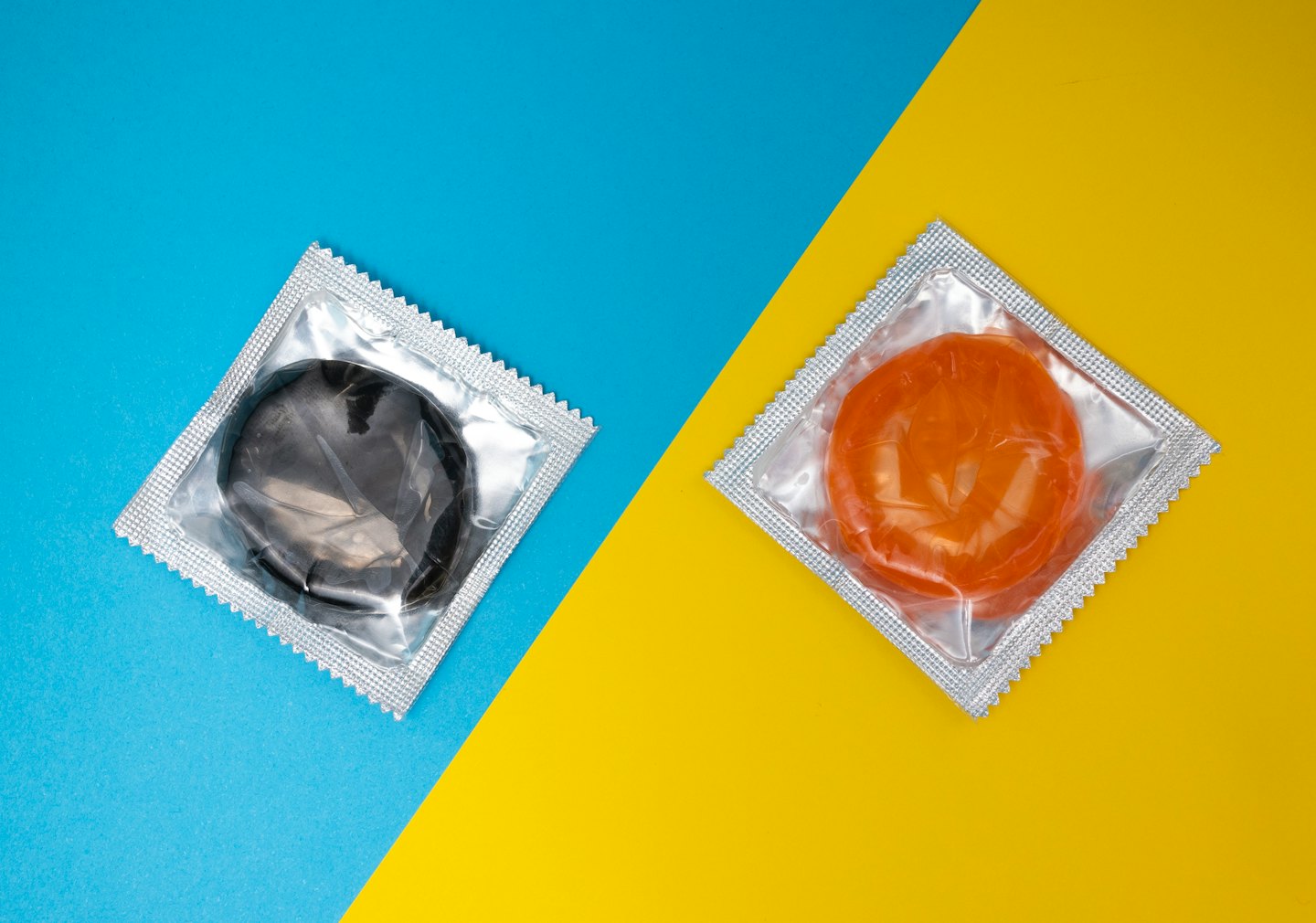 Twee condoompjes in folie op een blauw-gele achtergrond.